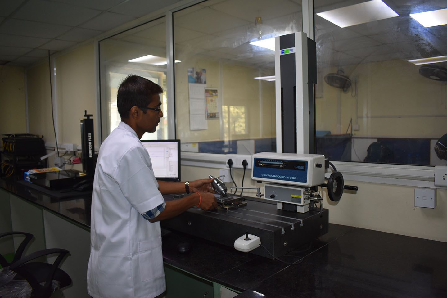 An inspector setting a component on the contour tracer in the PSCPL metrology lab, with the surface roughness tester behind