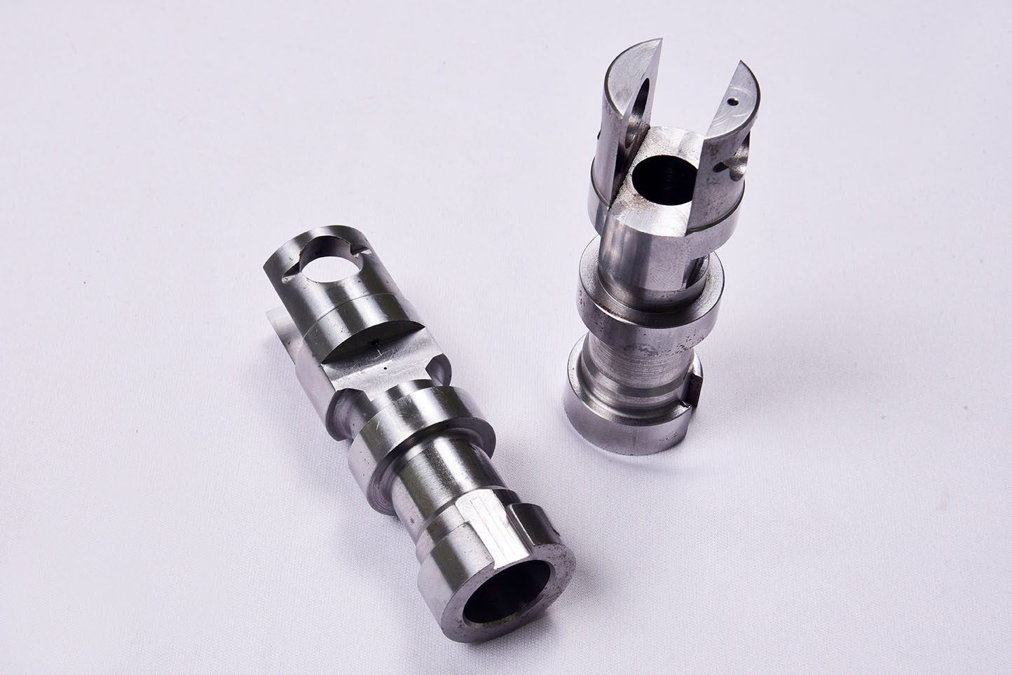 Two steel transmission spool components, slotted and cross-drilled, on a white ground